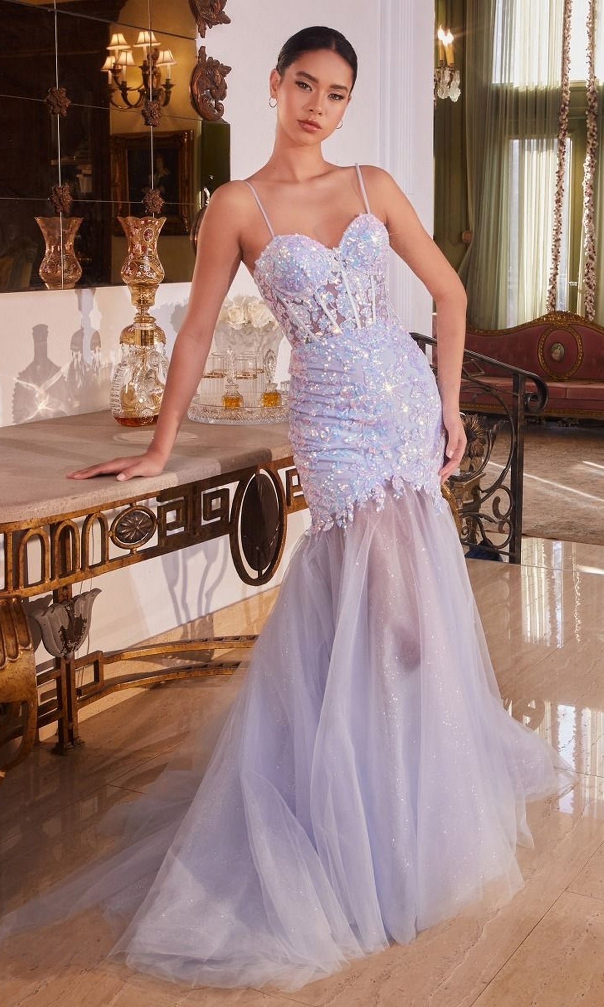 A woman poses indoors in the Long Blue Sequin Mermaid Prom Dress CB148, featuring a fitted silhouette and sparkling sequins, standing by an ornate console table with glass decanters.